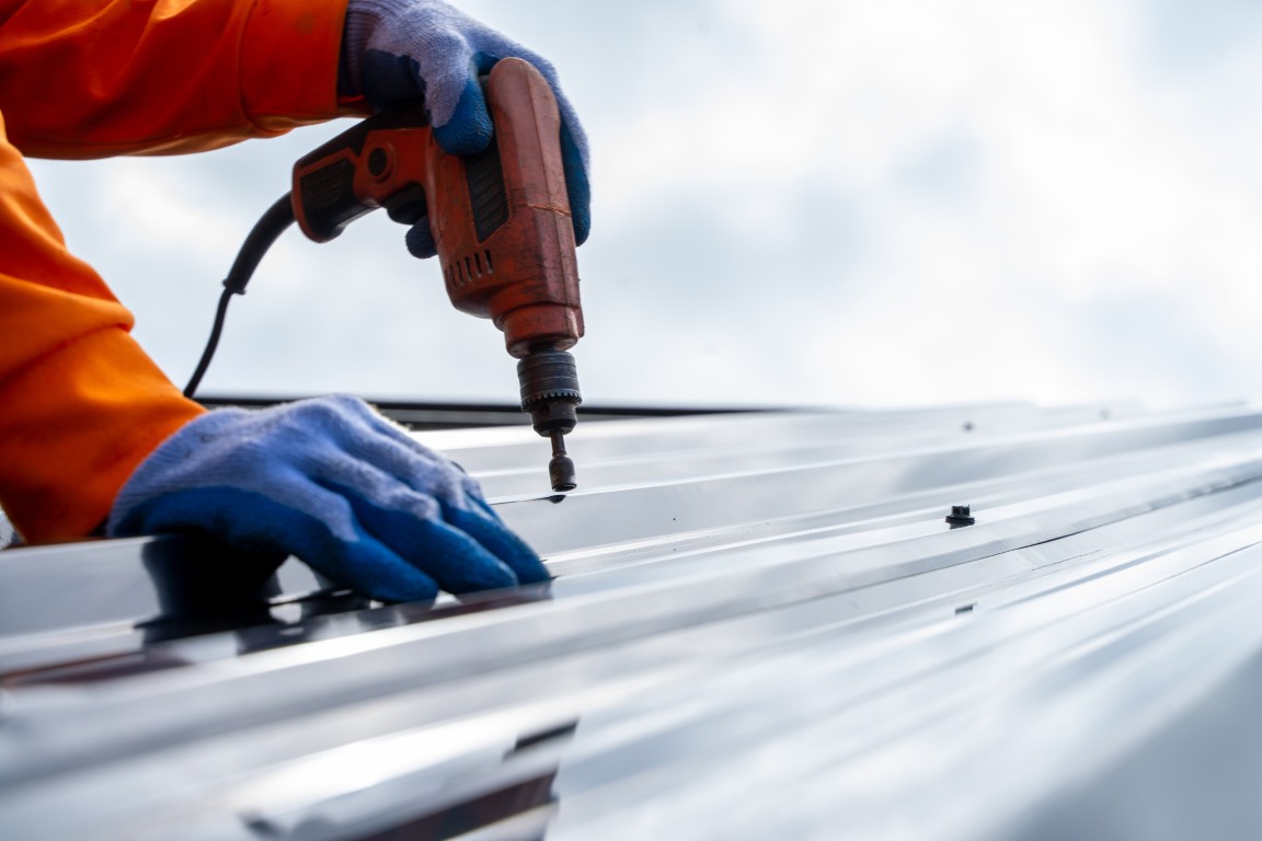 Close-up of worker installing exposed fastener metal roofing panel with power drill — highlighting precision and durability in metal roof installation.
