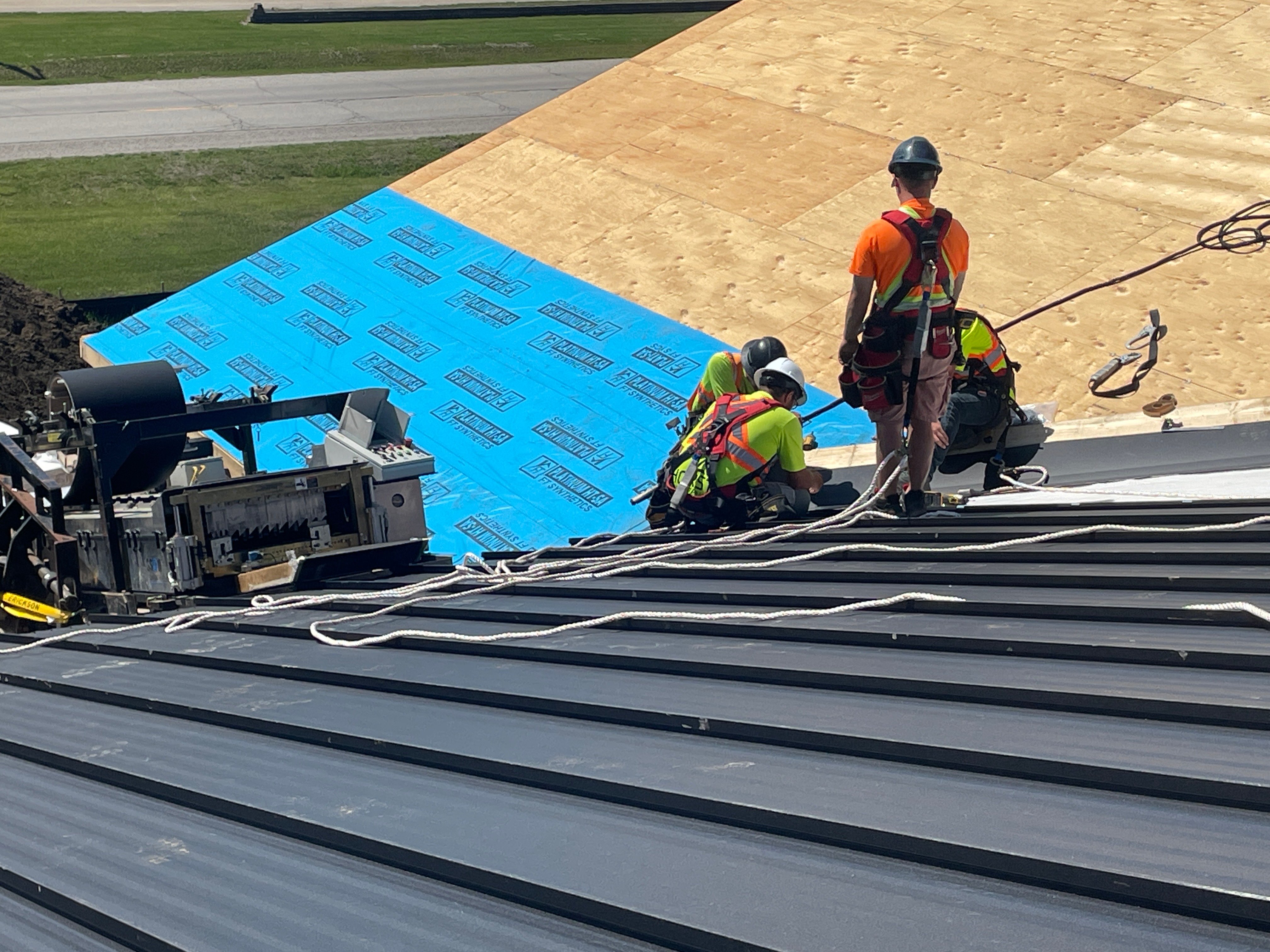 CountryTowne crew installing standing seam metal panels rolled on-site — showcasing custom roofing fabrication and safety harness use.