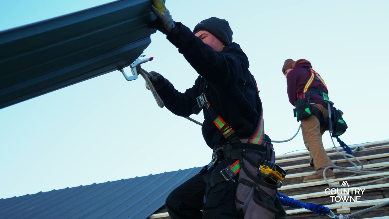 Installer fastening dark metal roofing panels on a Crown Rise Construction project