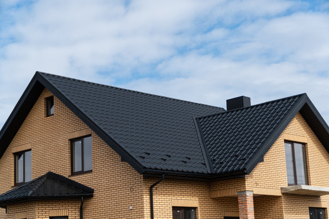 Angled view of a modern yellow brick home featuring black metal tile roofing with clean ridge lines and dormer accents