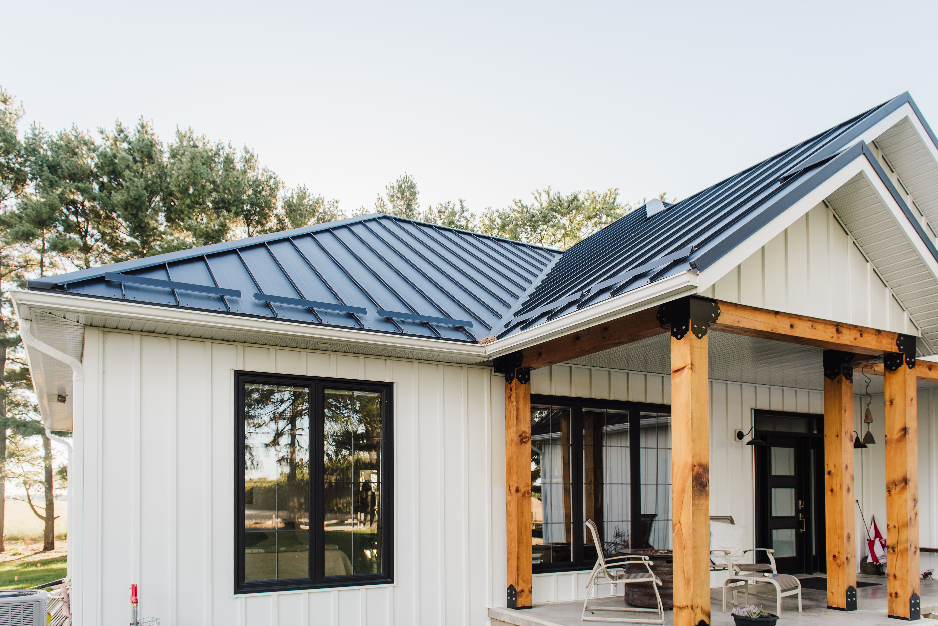 White board and batten house featuring a black standing seam metal roof with exposed wood posts and matte black window frames, showcasing contemporary rural architecture