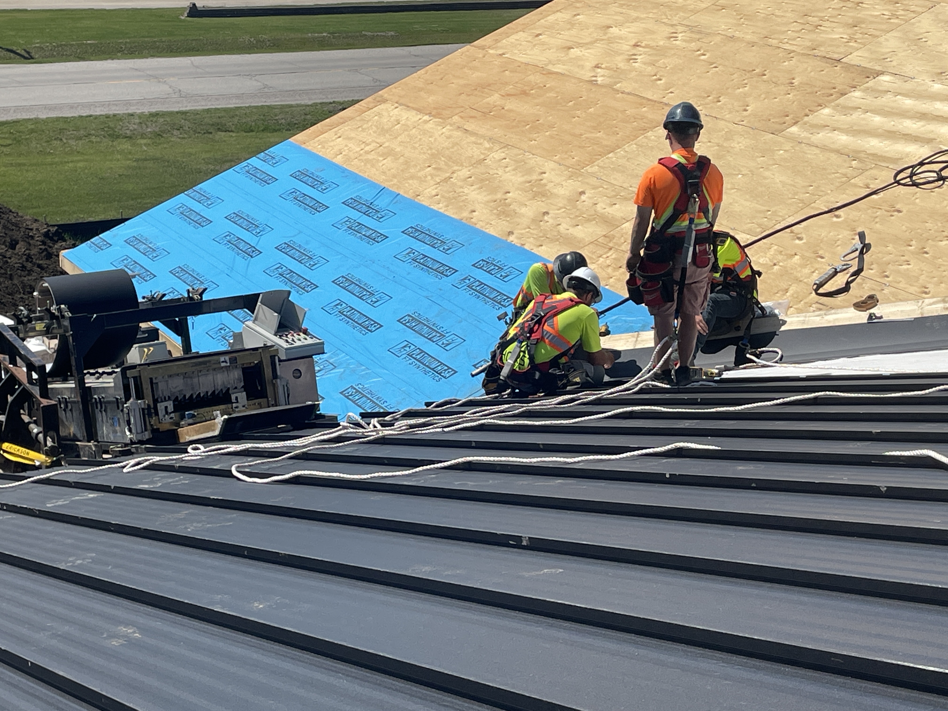 CountryTowne crew installing standing seam metal panels rolled on-site — showcasing custom roofing fabrication and safety harness use.