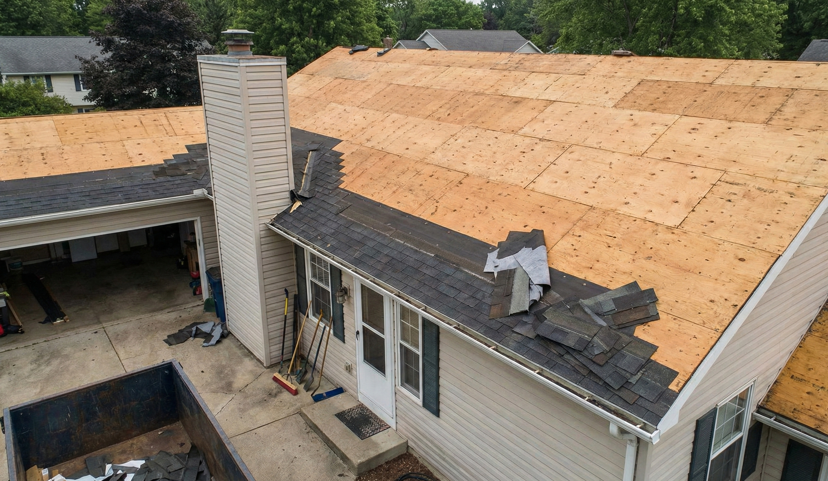 Residential roof with asphalt shingles removed, exposing plywood roof deck during tear-off before new metal roof installation