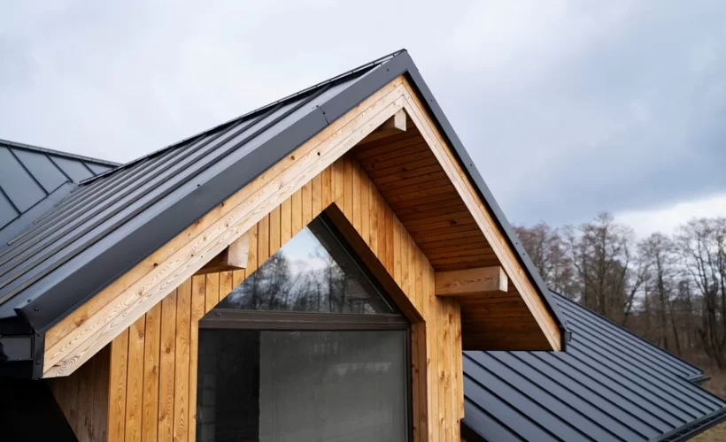 Close-up of a gable roof featuring black standing seam metal panels and natural cedar siding, highlighting modern rustic architecture with clean lines and warm wood tones