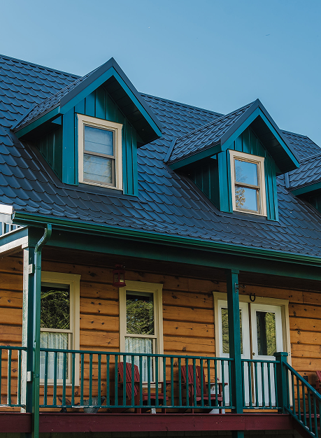 Detailed view of a green metal roof with standing seam panels and dormers on a rustic log-style cabin with wood siding and green trim